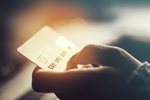 Person holding a credit card in front of a blurred background, focusing on the action of paying with a smartphone.