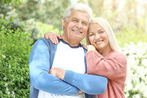 A man and a woman are embracing each other in a garden setting, with the man wearing a blue shirt and the woman in red.