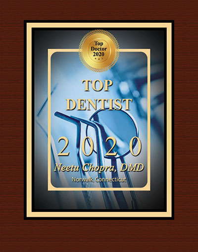 The image shows a plaque or award with a photograph of a dental chair and a pair of glasses, indicating recognition for a dentist. It features text that reads  TOP DENTIST 2020  and includes the name  NEENU CHOPRA MD.