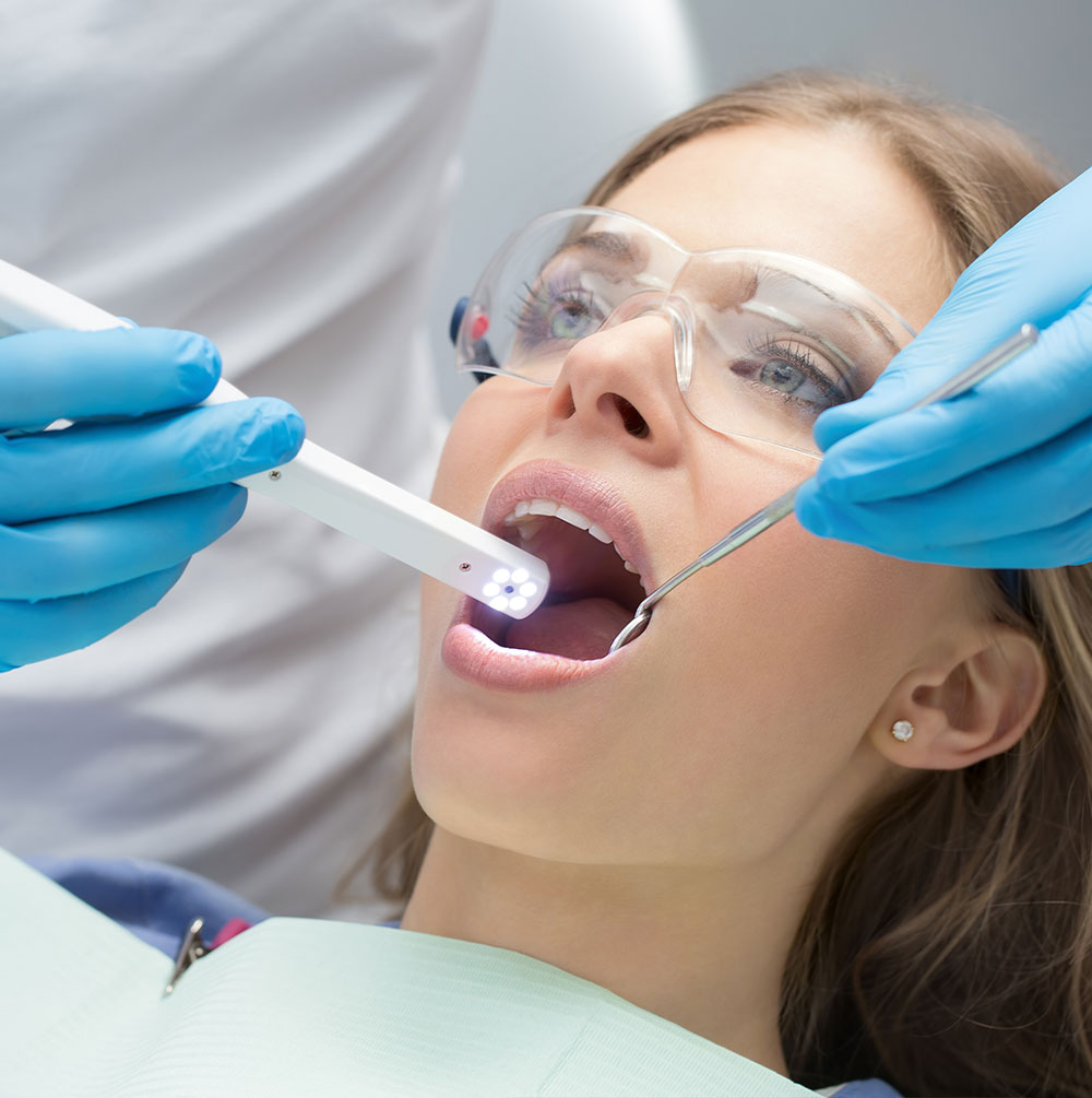 A woman in a dental chair with a dental professional using a device to examine her teeth.