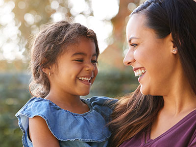 The image depicts a woman and a young child, both smiling and looking at the camera.