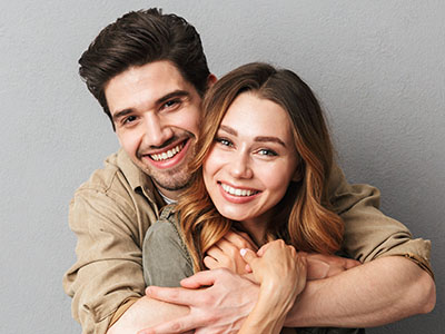 A young couple in a warm embrace, with the man wearing a blue shirt and the woman in a brown top.