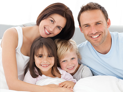 A family of four, including an adult couple and two children, sharing a joyful moment together in bed.