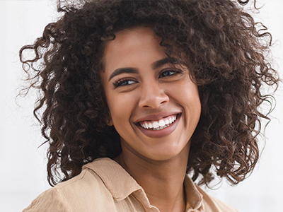 The image features a woman with curly hair, smiling at the camera. She appears to be a young adult and is wearing a brown top.