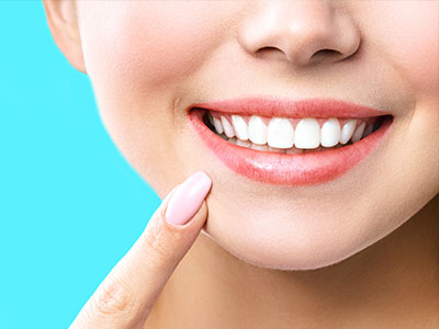 A smiling woman with a clear complexion, showcasing her teeth and lips, against a light blue background.